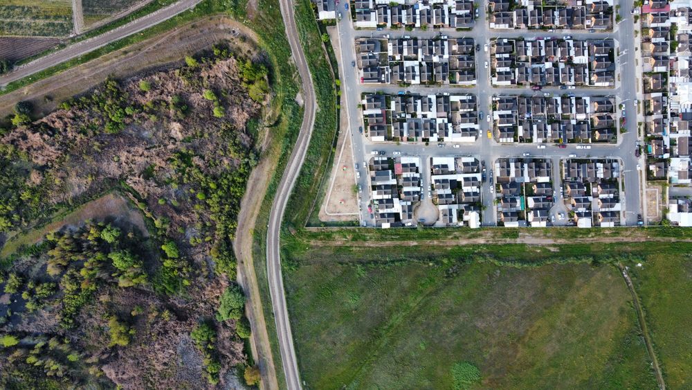 Drone view of a residential neighborhood alongside a natural landscape, showcasing urban and rural contrast