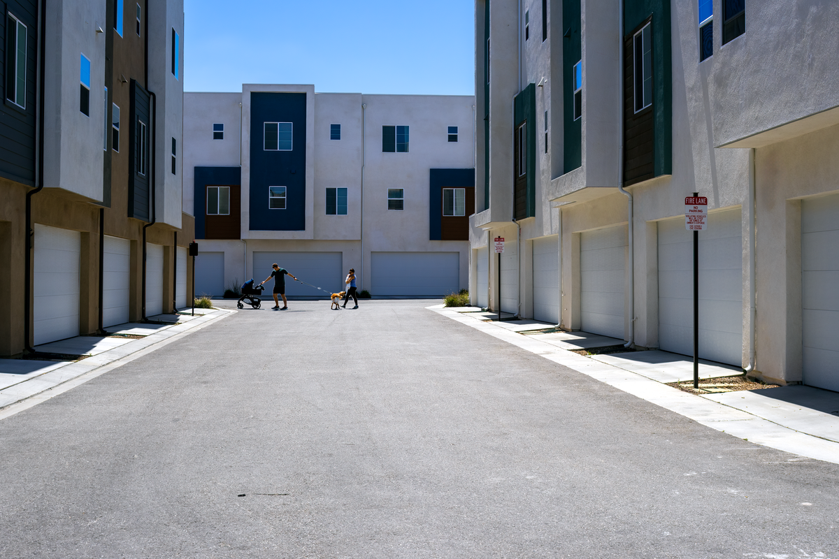 A quiet urban alley framed by sleek modern residential buildings under a summer sky